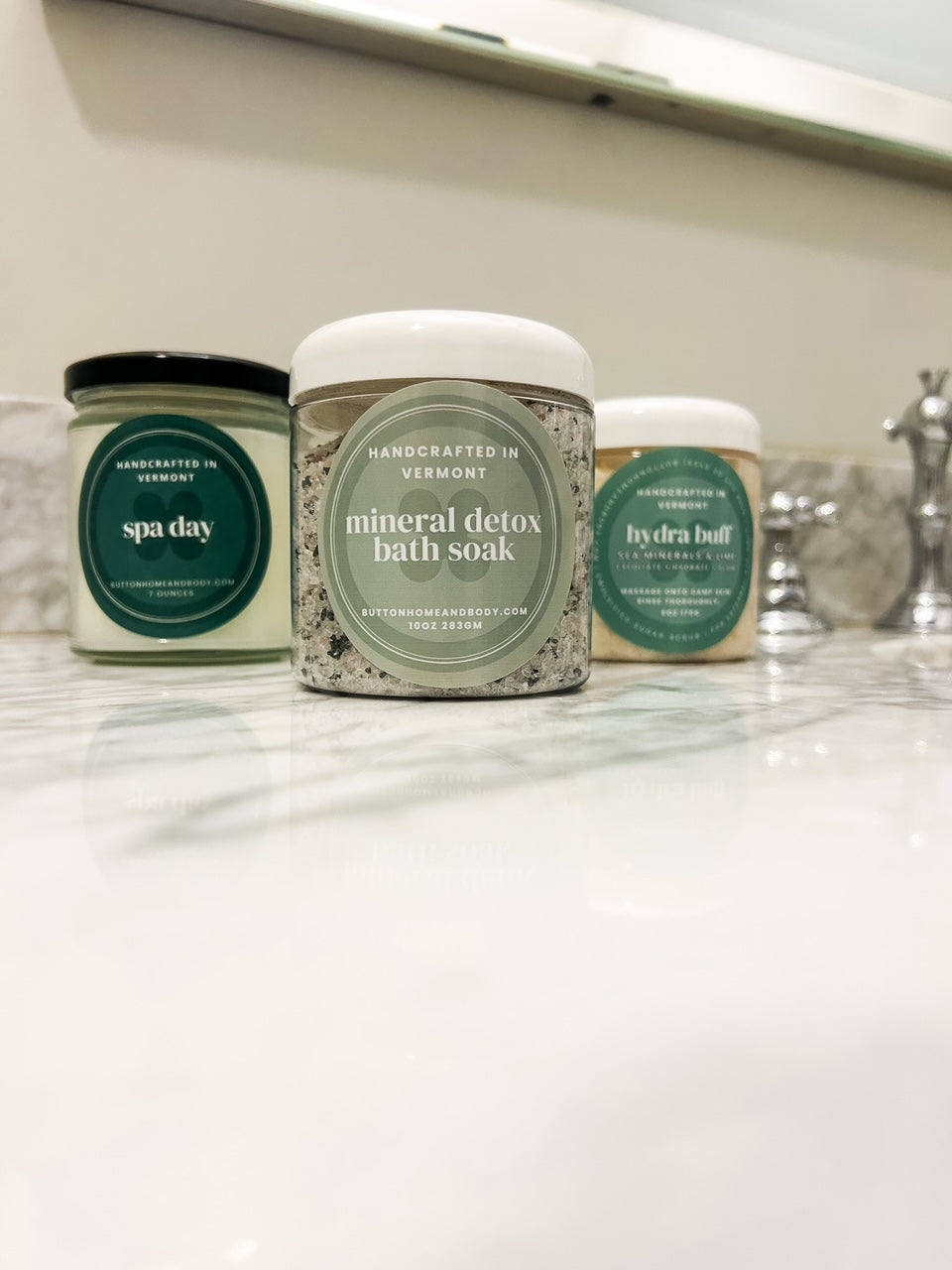 three products sitting on marble counter bath soak a candle and body scrub