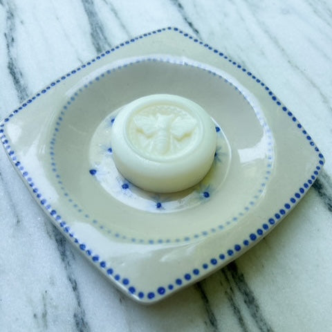 White solid lotion bar on a blue-rimmed white plate with a floral design on a marble surface