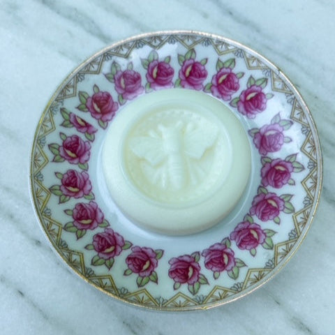 White solid lotion bar in a decorative holder with pink floral pattern on a marble surface