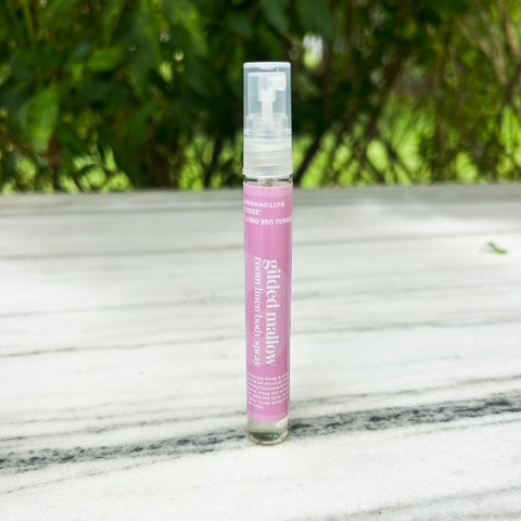 Pink spray bottle with a white label on a marble surface with greenery in the background