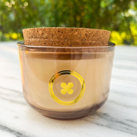 Glass container with cork lid on a marble surface with greenery in the background