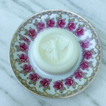 White solid lotion bar in a decorative holder with pink floral pattern on a marble surface