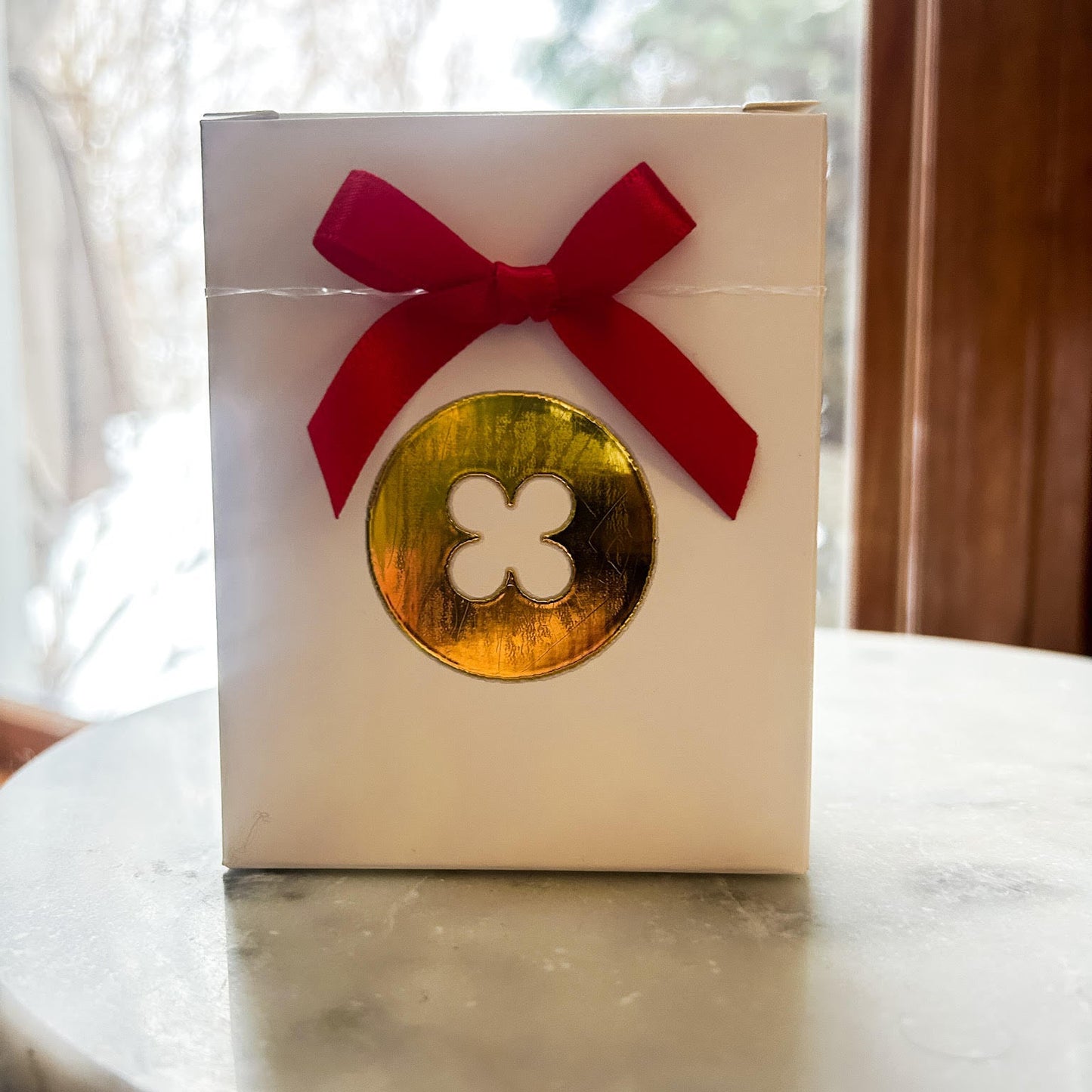 White box with a gold button and red bow on a marble surface