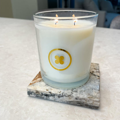 White candle with a gold logo on a marble coaster