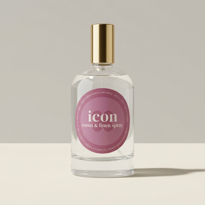 Icon room and linen spray with a mauve oval label and gold cap against a soft gray background.