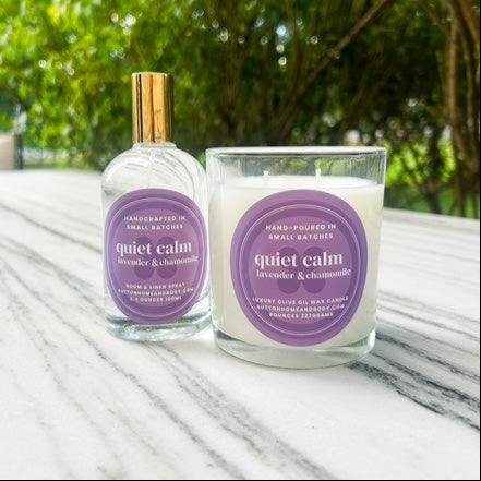 Bottle and candle labeled 'quiet calm' on a marble surface with greenery in the background